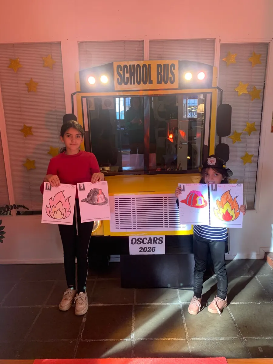 Alunos segurando cartazes em frente ao ônibus escolar decorado para o Oscars 2026