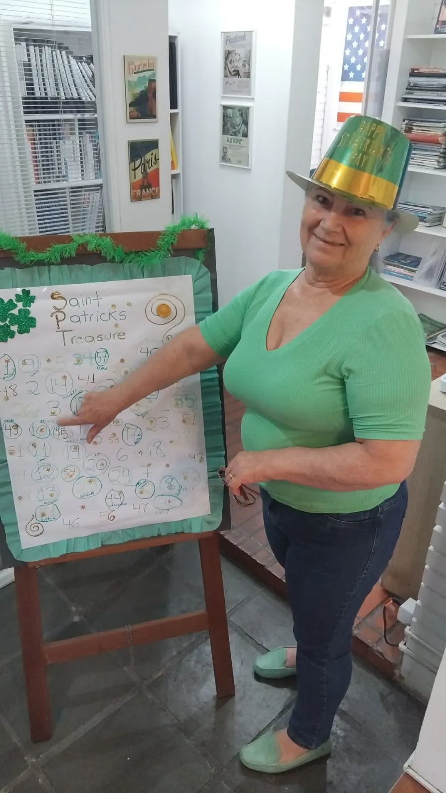 Senhora de chapéu verde apontando o quadro do St. Patrick's Day na School House